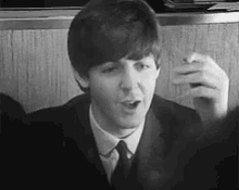 a black and white photo of a young man in a suit and tie smoking a cigarette .