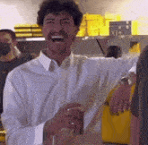 a man in a white shirt is laughing and holding a cup