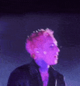a man with pink hair is singing into a microphone in a dark room .