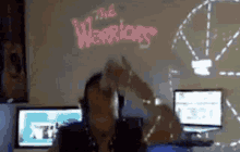 a man is standing in front of a microphone in front of a wall with the words `` the warriors '' written on it