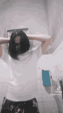 a woman in a white shirt is dancing in a bathroom