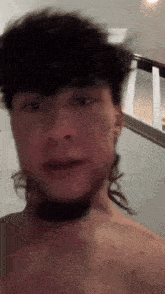 a man with long hair and a beard is standing in front of a staircase without a shirt on .