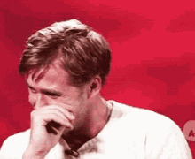 a man covering his mouth with his hand in front of a red background .