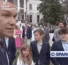 a man in a suit and tie is standing next to a group of children .