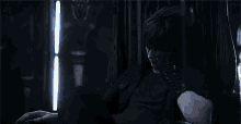a man in a black suit is sitting in a dark room