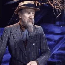 a man with a beard and a hat is wearing a striped suit .