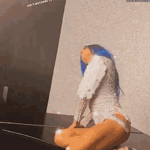 a woman with blue hair is kneeling down in front of a wall wearing a white dress .
