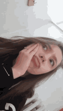 a girl with long hair and a ring on her finger is covering her face with her hand .