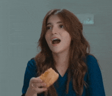 a woman in a blue shirt is eating a piece of bread .