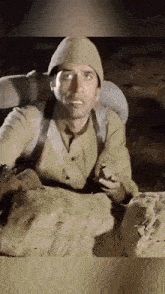 a man in a military uniform is sitting in a trench holding a cigarette .