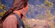 a man with long hair and a bandana on his face is walking through a forest .