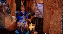 a woman in a blue and white feathered dress is standing in a room next to a window .
