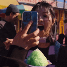 a woman taking a picture of a shaved ice with a phone