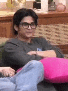 a man wearing glasses is sitting on a couch with two pink pillows .