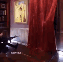 a man is holding a gun in a room with a red curtain and a picture on the wall .