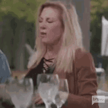 a woman is sitting at a table with wine glasses and talking to someone .