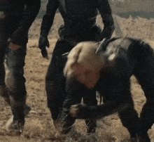 a woman in a black suit is kneeling down in the dirt