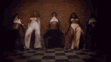 a group of women are dancing in front of a brick wall in a room .