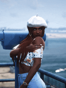a woman wearing a white hat and a floral top stands on a balcony overlooking a body of water