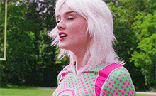 a woman with white hair is wearing a pink and green shirt with polka dots on it .