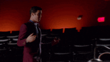 three people are sitting in an auditorium with a red exit sign behind them