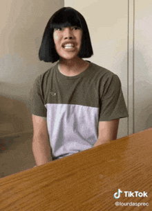 a man with a wig on his head is sitting at a table with a tiktok sticker