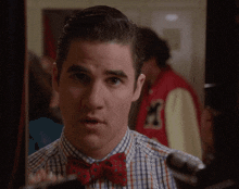 a man wearing a plaid shirt and a red bow tie looks at himself in the mirror