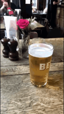 a glass of beer with the letter be on it sits on a wooden table
