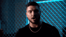 a man with a beard is singing in front of a chain link fence in a dark room .