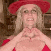 britney spears is wearing a red cowboy hat and making a heart shape with her hands .