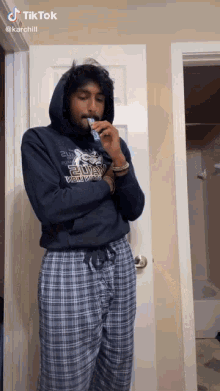 a man in a hoodie and plaid pajama pants is smoking a cigarette .