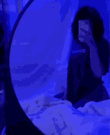 a girl is sitting on a bed taking a picture of herself with her phone .