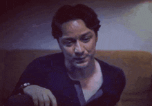 a man in a blue shirt is sitting on a couch with his hand on his knee .