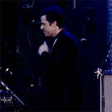 a man in a black suit stands in front of a drum set in a dark room