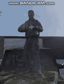 a man in a camouflage jacket is standing in front of a truck holding a gun .
