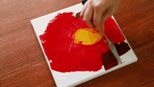 a person is spreading red and yellow paint on a white canvas
