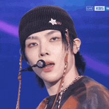 a close up of a person wearing a beanie with a star on it and a kbs logo in the background
