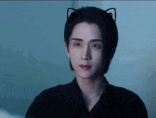 a young man with cat ears on his head is wearing a black shirt and looking at the camera .