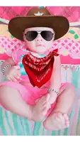 a baby wearing a cowboy hat and sunglasses is sitting on a bed