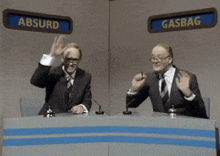 two men are sitting at a desk with a sign that says absurd and gasbag