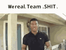 a man in a black shirt is standing in front of a house with the words `` we real team shit '' above him .