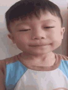 a young boy is making a funny face with his eyes closed and a rainbow on his shirt .