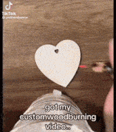 a person is making a heart with a hole in it and says " got my custom woodburning video "