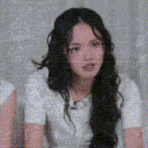 a woman with long hair is wearing a white shirt and looking at the camera .