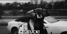 a black and white photo of a man standing next to a white car with the word fuck written on it