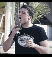 a man wearing a black shirt that says clermont lounge is holding a cell phone in his mouth