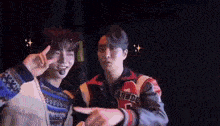 two young men are standing next to each other in a dark room and making a peace sign .