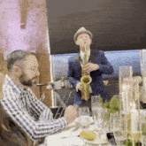 a man is playing a saxophone while a man sits at a table
