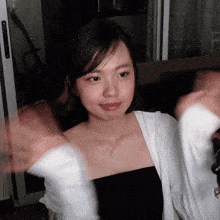 a woman wearing a black top and a white cardigan is waving her hands