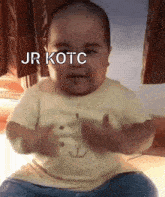 a baby is sitting on a bed with the words jr kotc written above him